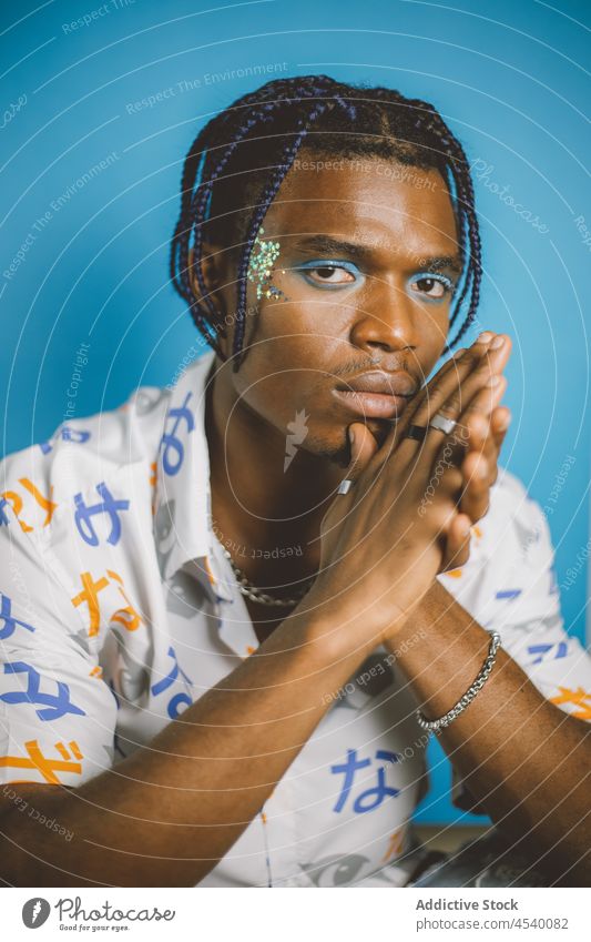 Black man with colorful makeup alternative style appearance queer eccentric fashion extravagant informal serious confident hairstyle braid male african american