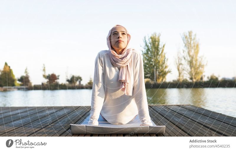 Peaceful Arab woman doing yoga on embankment asana waterfront river practice exercise healthy lifestyle female arab muslim headscarf hijab shore mindfulness