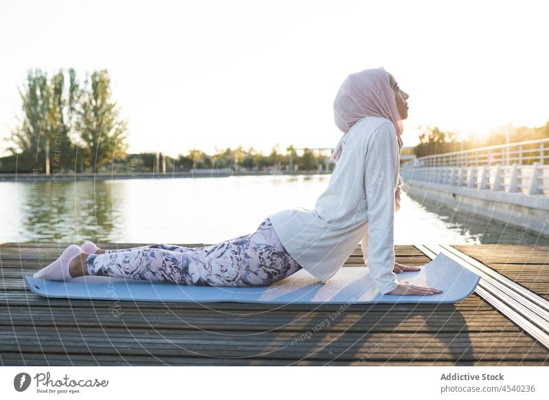 Peaceful Arab woman doing yoga on embankment asana waterfront river practice exercise healthy lifestyle female arab muslim headscarf hijab shore mindfulness