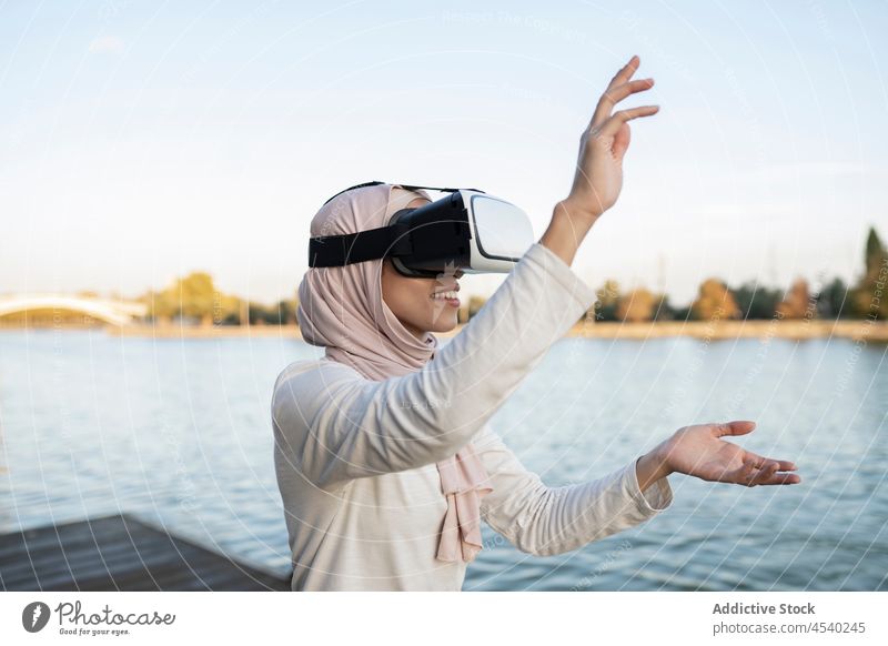 Arab woman in VR headset on embankment vr goggles virtual reality river simulate cyberspace water female arab muslim waterfront modern contemporary headscarf