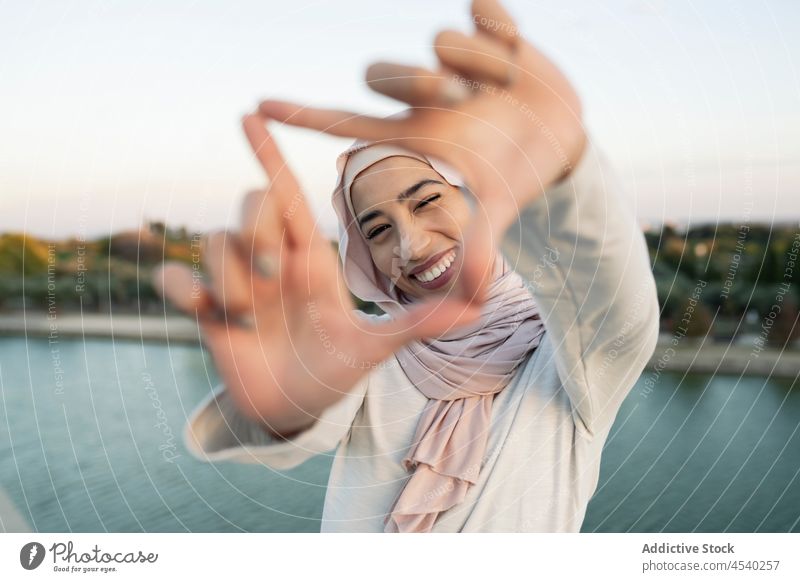Cheerful Arab woman doing frame gesture on embankment waterfront hijab river leisure shore pastime riverside female arab muslim lady summer smile content
