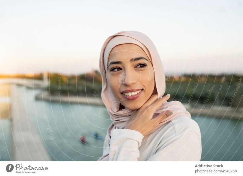 Portrait of cheerful Arab woman on embankment waterfront hijab river leisure pastime riverside shore railing barrier thirst female text message arab muslim