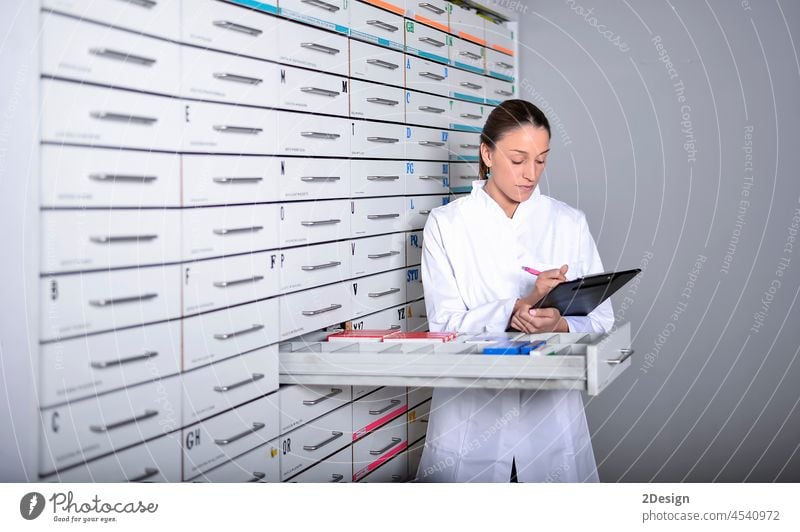 Young pharmacist standing next to medicine shelves, holding tablet uniform medication work health apothecary female pharmacy pretty woman beautiful 1 care