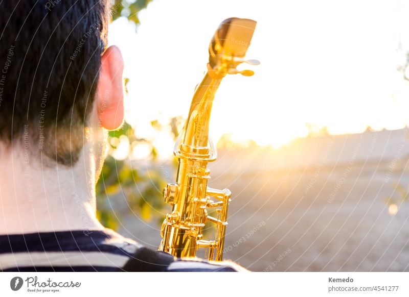 Man holding a saxophone during a sunset in natural outdoor place. copy space sunny sunlight saxophonist music musical instrument play musician nature village