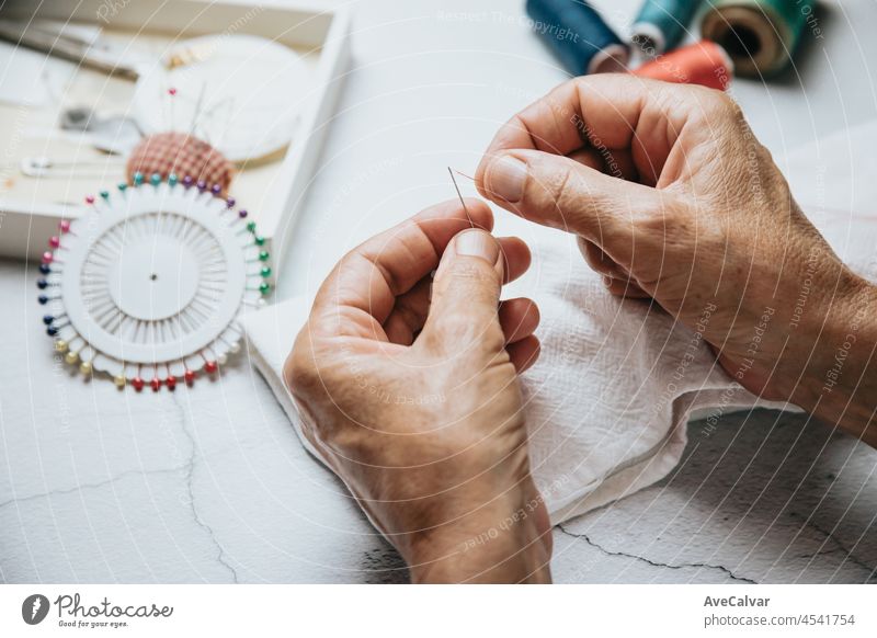 Seamstress old hands sewing and doing works. Cloth working and sewing. Lightful image, copy space, threads of different colors background. Cutting cloth senior