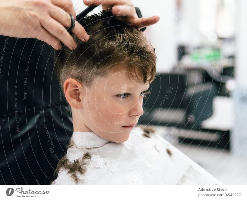 Hair stylist cutting hair of boy in salon client haircut scissors positive process procedure work coiffure cape apron kid professional tool service hairstylist