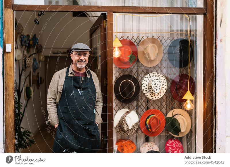 Mature male owner standing near entrance of fashionable hat shop man showcase master handmade collection small business style store sale merchandise tradition