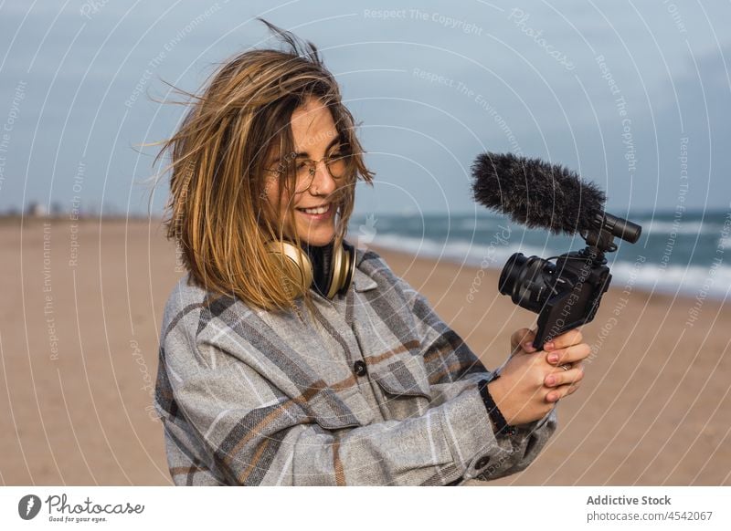 Young lady on seashore and shooting video on camera woman beach vlog record cheerful blogger photo camera ocean vacation happy sand female young millennial
