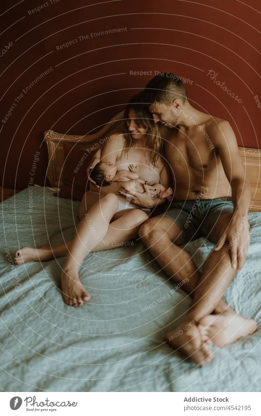 Happy naked couple with baby cuddling on bed family cuddle newborn kiss breastfeed love together embrace relationship happy close wife husband adult nude care