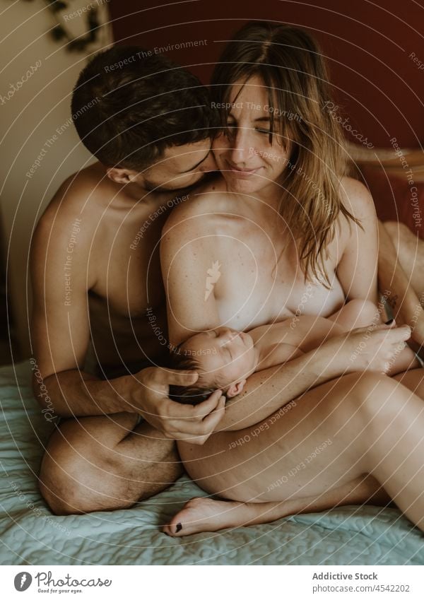 Happy naked couple with baby cuddling on bed family cuddle newborn kiss breastfeed love together embrace relationship happy close wife husband adult nude care