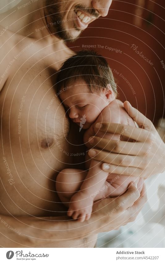 Anonymous shirtless Hispanic man hugging cute baby in bedroom newborn embrace father love care fatherhood affection together tender parent male young ethnic