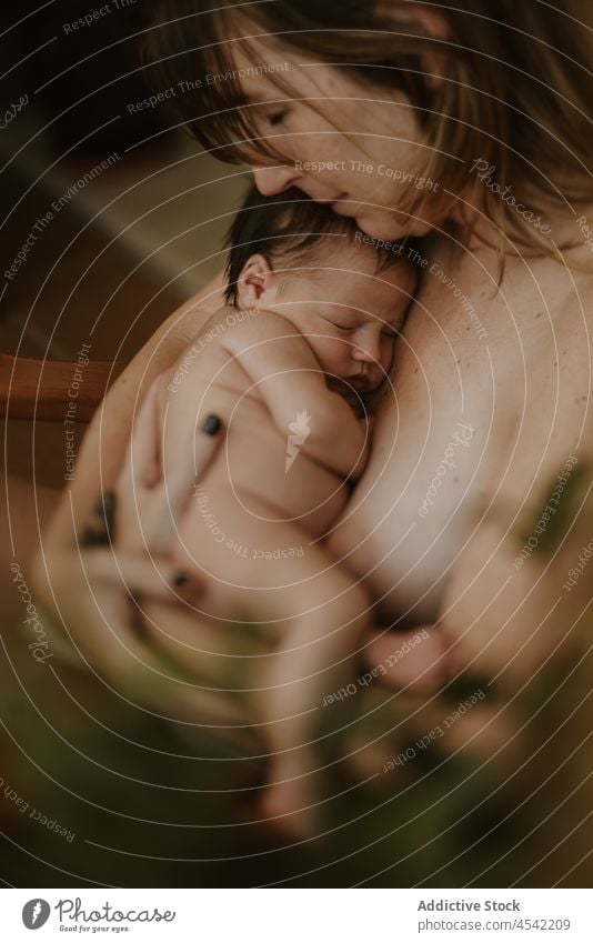 Young barefooted mother hugging baby while sitting on chair woman embrace newborn breastfeed love naked together motherhood childhood nude female young home