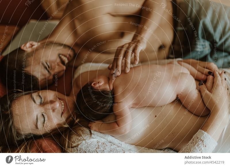 Happy naked couple with baby cuddling on bed family cuddle newborn breastfeed love together embrace lying down relationship happy wife husband nude care tender