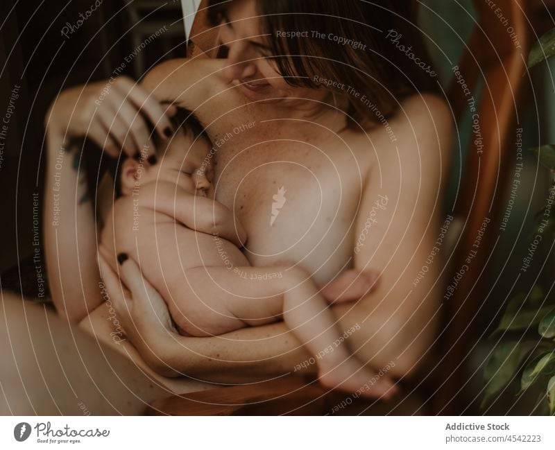Smiling mother hugging baby while sitting on chair woman embrace newborn breastfeed smile love delight naked together motherhood childhood nude female young