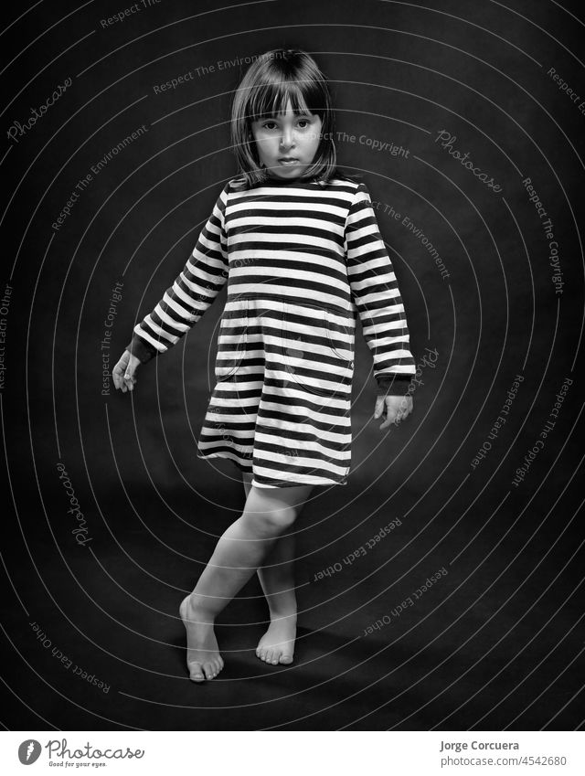 4-year-old girl posing elegantly in a black and white striped dress. Monochrome solid black background. 4-5 years alternative pose baby girls beautiful people
