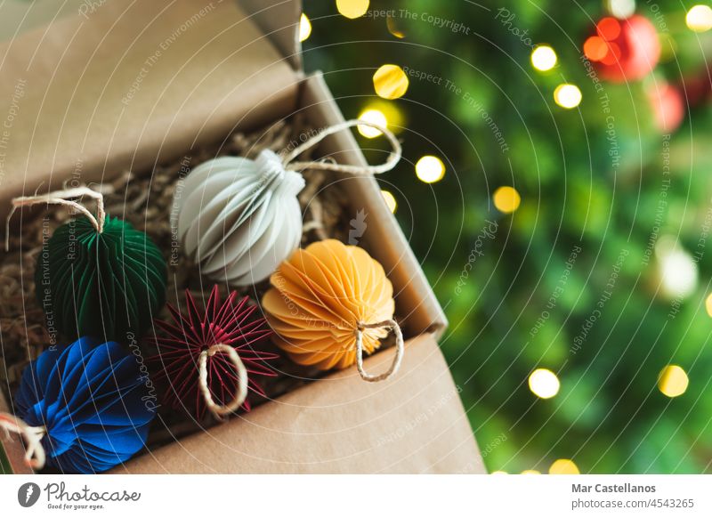 Christmas ornament balls in box with tree and lights in the background. Copy space. ornaments paper cardboard hand open copy homemade rope handmade fasten