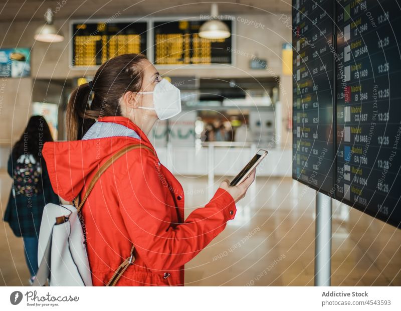 Woman in medical mask browsing on mobile phone near timetable in airport woman traveler trip terminal departure schedule signboard protective pandemic epidemic