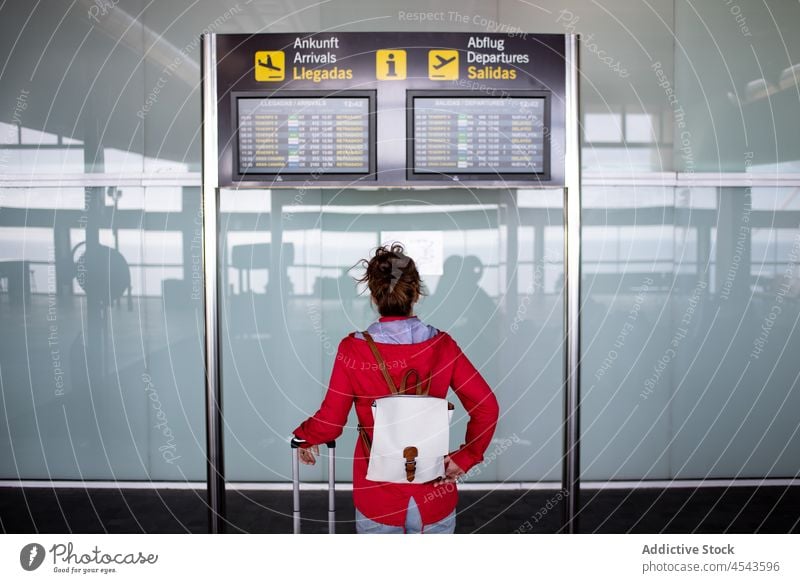 Unrecognizable traveler sitting near timetable in airport woman trip modern terminal departure journey signboard public contemporary luggage tourist