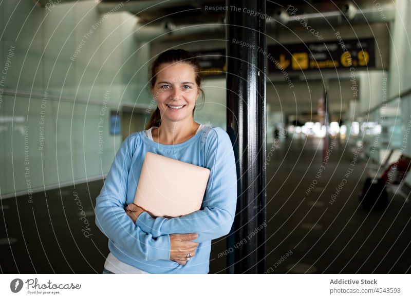 Cheerful woman with laptop in airport traveler trip terminal departure journey public passenger contemporary tourist infrastructure modern style international