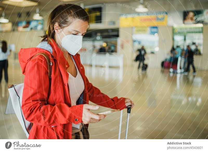 Woman in medical mask browsing smartphone in airport woman online traveler trip departure suitcase new normal protective coronavirus covid 19 terminal journey
