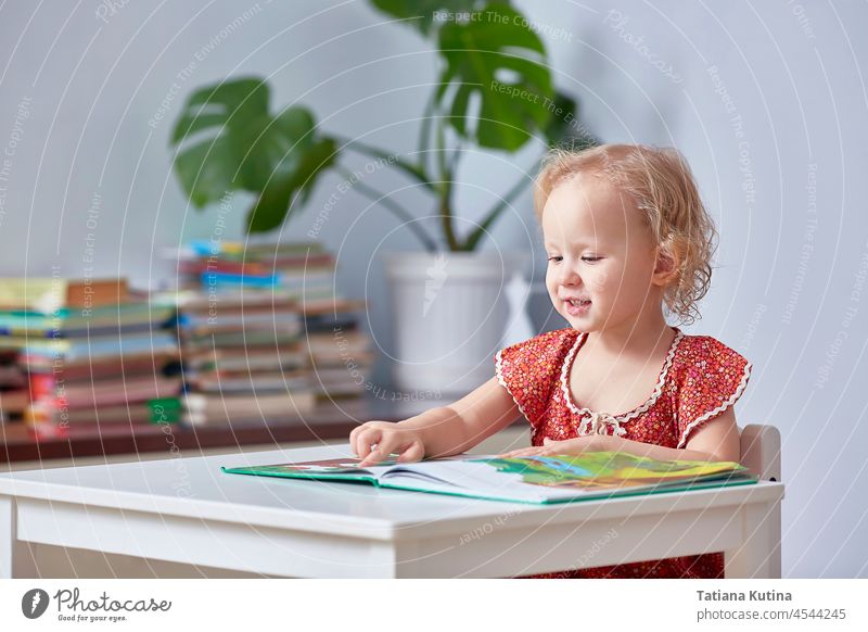 A cute girl is reading a children's book and holding a finger. baby learning home todler preschooler curly kid happy little young education studying people