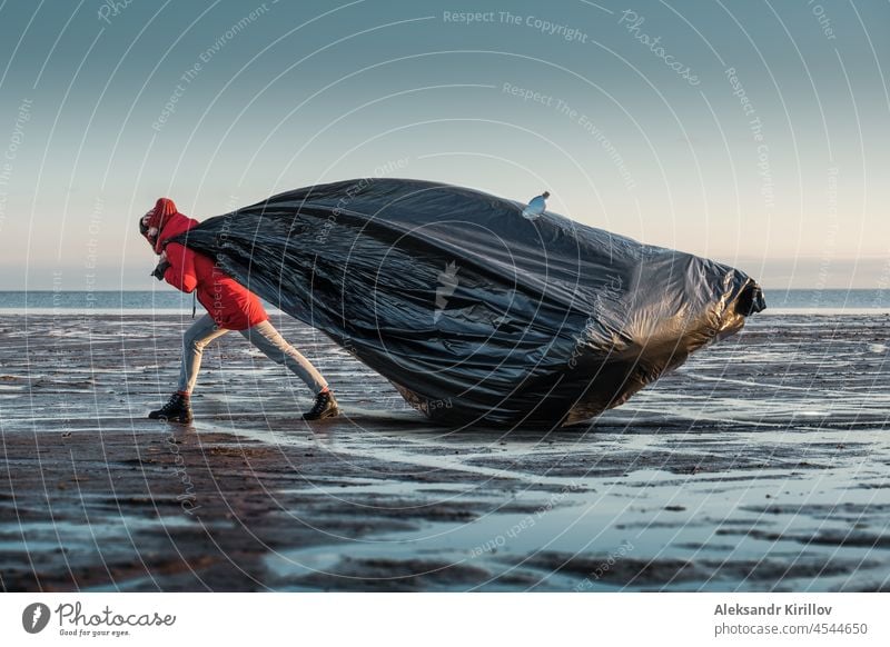 A woman drags a huge black trash bag along the shore ecology plastic bottles collection cleanup threat pollution recyclable environmental threat waste nature