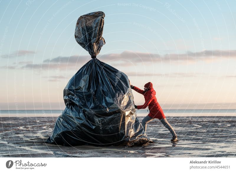 A woman pushes a huge black trash bag on the shore ecology plastic bottles collection cleanup threat pollution recyclable environmental threat waste nature lake