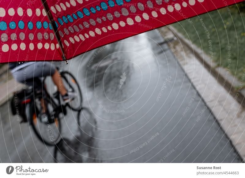A cyclist passes a walker with a dotted umbrella in the rain. Rain Umbrella cyclists Red Street reflection polka-dot umbrella summer rain Bad weather