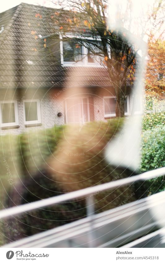 Blurred silhouette of a woman behind a window in which the neighboring house is clearly reflected Woman Young woman short hair Brunette look naturally Authentic