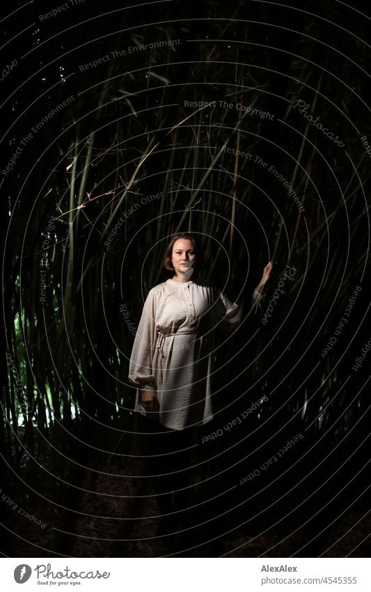 Portrait of a young woman in the park in a dark bamboo forest, light from the side Beige Green Moody Face of a woman free time Self-confident naturally real