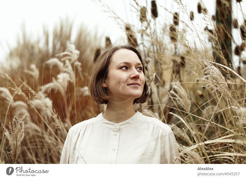 Portrait of a young smiling woman in the park in autumn in front of dry grasses Cheerful Ease Beige Green Beautiful weather Moody Face of a woman free time