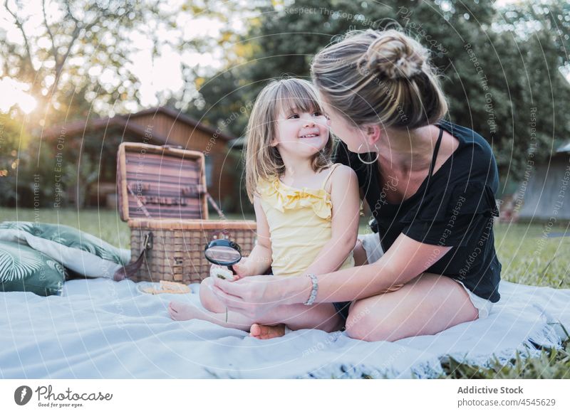 Happy mother and daughter examining bug with magnifying glass during picnic woman child hug examine insect together interest nature parent young kid blond