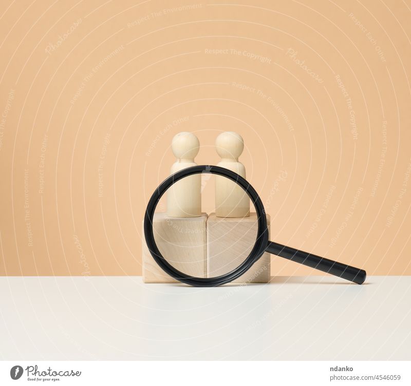 wooden figures of men stand on a beige background and a red plastic magnifying glass. Recruitment concept, search for talented and capable employees, career growth