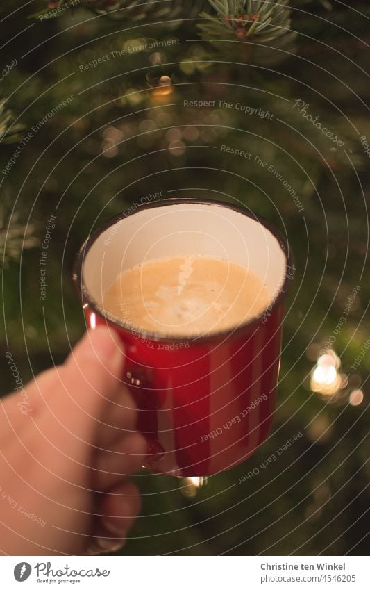 One hand holds a red cup with cappuccino. In the background fir green with shiny lights. Advent coffee. Coffee mug Cappuccino Hand To hold on stop Mug Cup