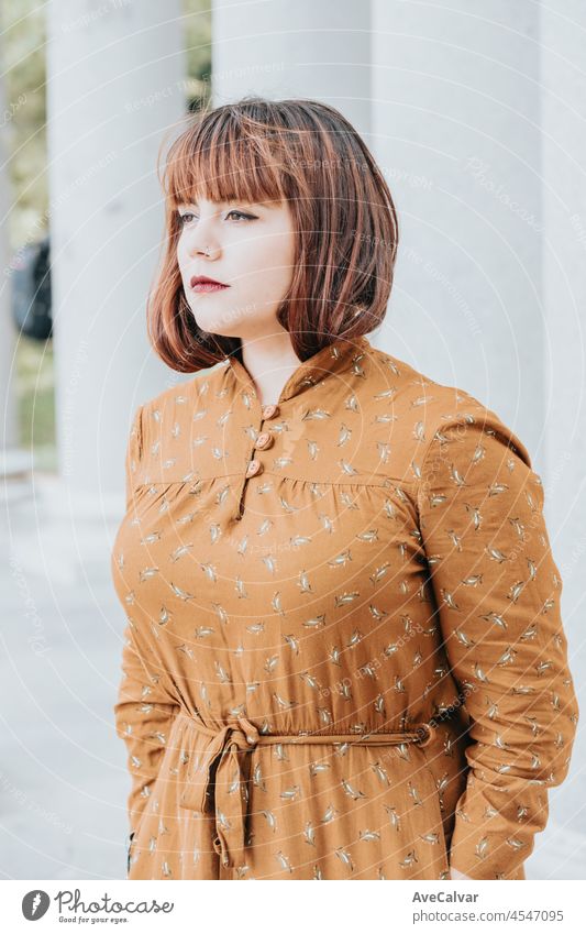 Modern serious pose portrait she her hipster redhead young woman. Copy space for text image. Casual dressing in autumnal tones. red lips and modern hairstyle, bright day. Body Positive