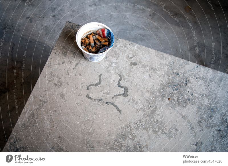 The workmen left a former yogurt cup full of cigarette butts after work Table stone slab factual sober Minimalistic Corner Wood grain texture Mug cigarettes