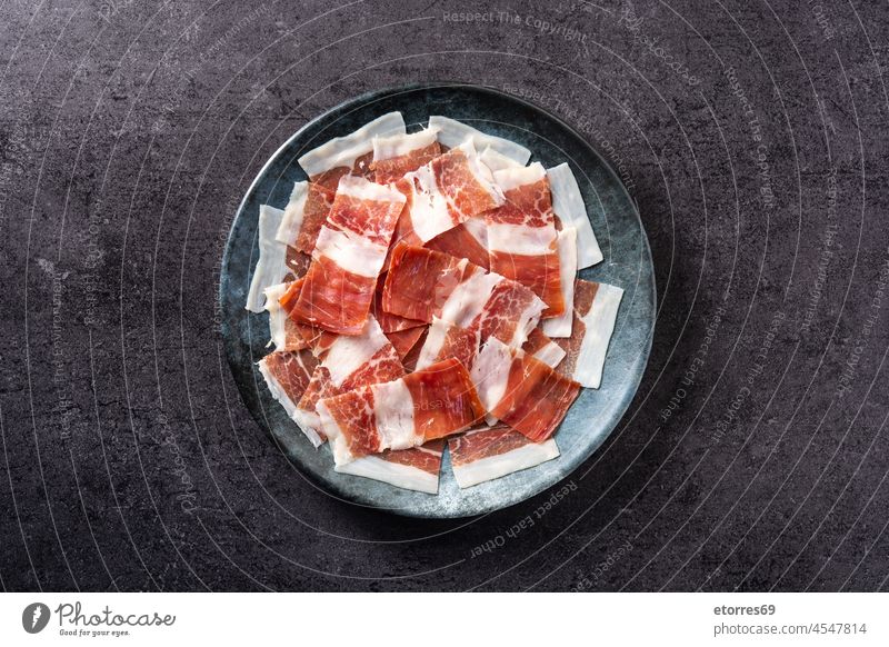 Spanish serrano ham slices on black plate on black background spanish prosciutto italian cold cuts food pork cured jabugo meat breakfast cutting board