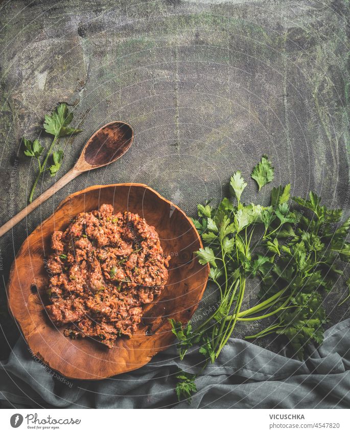Food background with meat stuffing on dark table with herbs, wooden cooking spoon and dish towel. Cooking with minced meat and parsley. Top view with copy space.