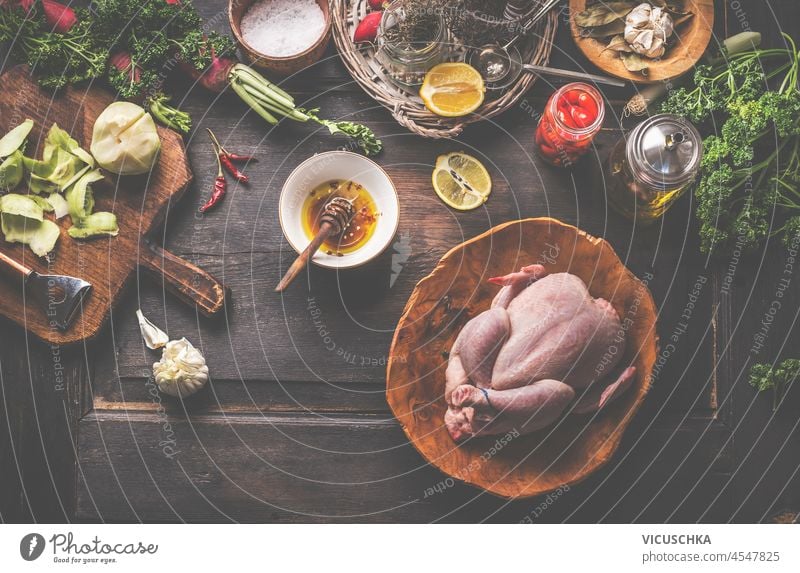 Raw whole chicken on rustic wooden table with marinade, garlic, apple, spices, jars and kitchen utensils. Cooking preparation at home with raw meat and flavorful ingredients. Top view.#