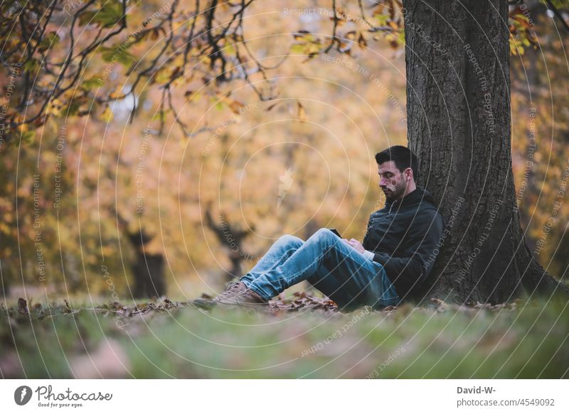 Man sits outside in nature by a tree and enjoys the silence Nature Tree rest To enjoy tranquillity Cellphone Hand relax time-out Autumn Autumnal gap