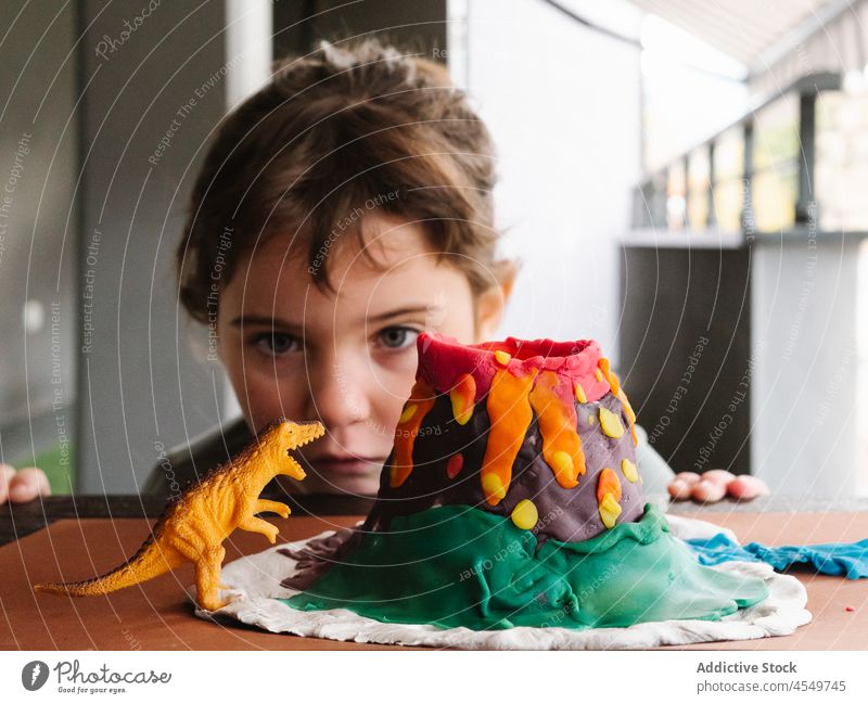 Little girl playing with toy dinosaur after sculpting plasticine volcano child little figurine figure childhood creative table balcony kid hand clay dough