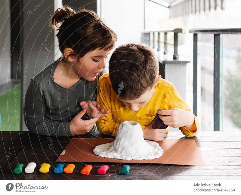 Concentrated kids molding plasticine while creating volcano figurine children play handmade childhood attentive brother sister craft clay boy girl handicraft