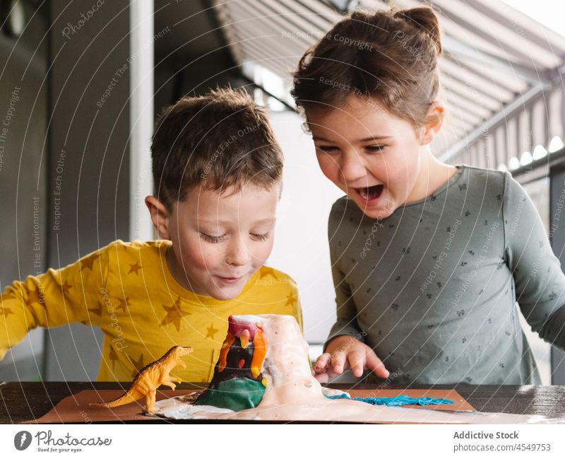 Amazed children playing with dinosaur toy and plasticine volcano amazed excited wow together brother sister astonish adorable surprise erupt sculpt kid casual