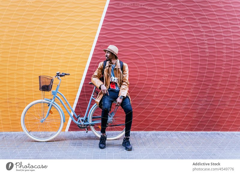Black man on bicycle near colorful wall street pastime bicyclist hobby leisure walkway street style garment wear appearance male black african american trendy