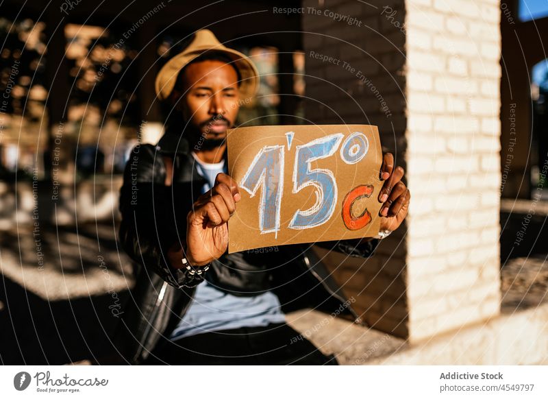 Black man showing paper with weather temperature celsius street city information notice sunshine demonstrate sunlight 15 wear town african american black hat