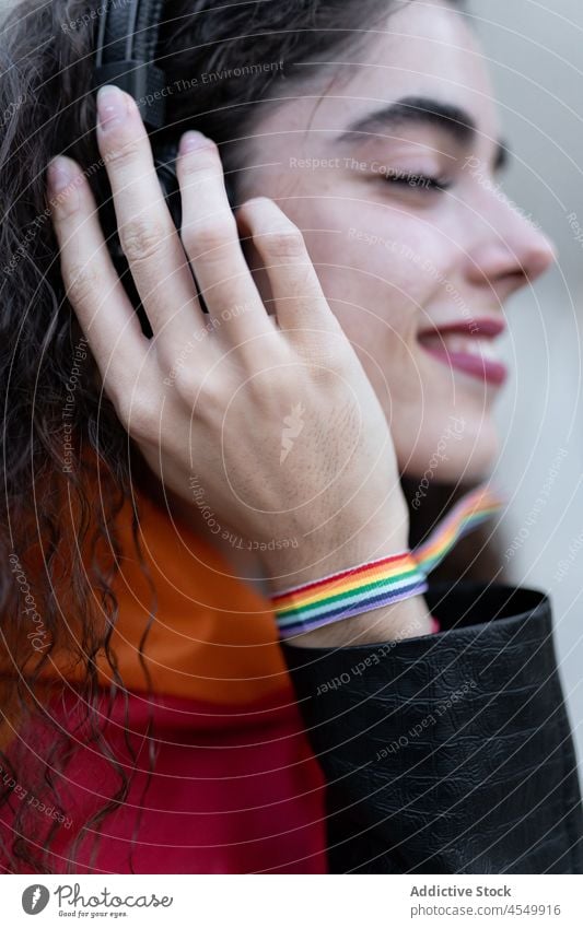 Cheerful Hispanic lesbian with LGBT bracelet listening to music lgbt woman headphones street homosexual equal unconventional meloman playlist song wireless tws