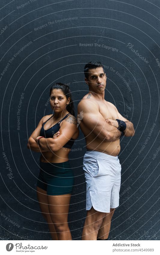 Serious Hispanic sportive couple near wall sportspeople training healthy lifestyle wellness fitness muscular workout arms crossed confident sportswoman serious
