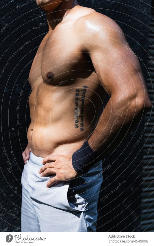 Anonymous positive shirtless Hispanic sportsman near wall training healthy lifestyle wellness fitness muscular naked torso street male sportswear sporty