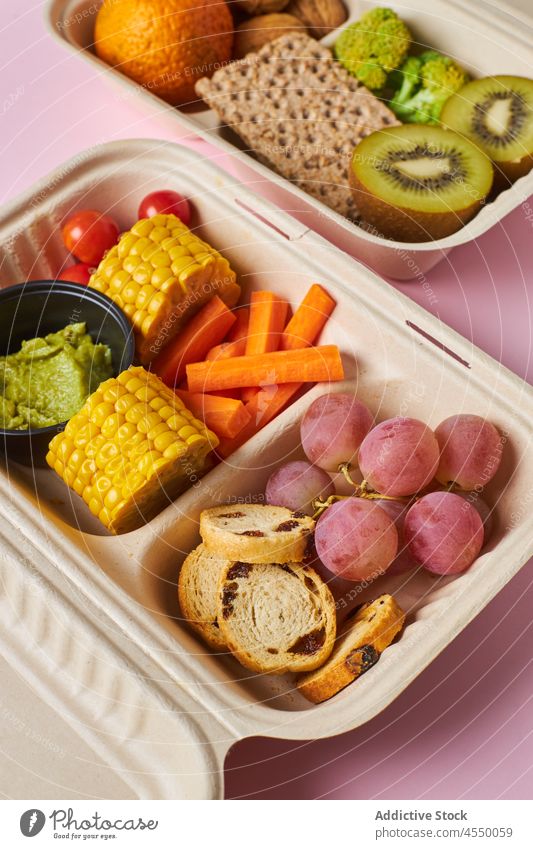 Opened containers with healthy snacks on table lunch box diet nutrition vegetable fruit kiwi grape walnut cracker berry food slice nutrient tangerine carrot