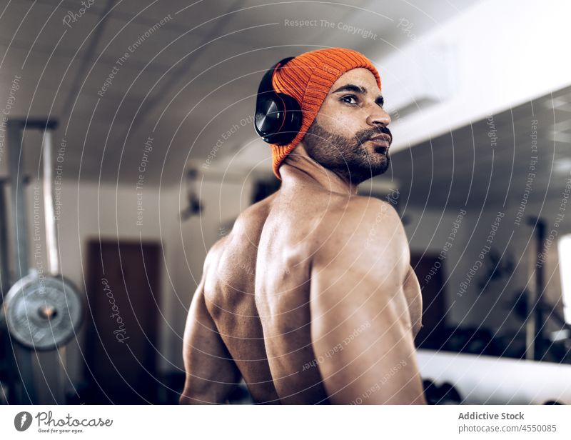 Muscular sportsman in hat and headphones in gym athlete muscular workout music listen wireless shirtless fitness male training muscle power wellness healthy